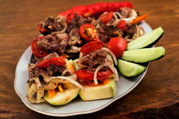 A plate with baked zucchini and eggplant, on which layers are laid fried meat with onions and tomatoes.