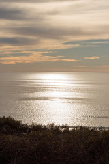 Shimmering ocean silver sun lit sunset view with blue sky and clouds in the background