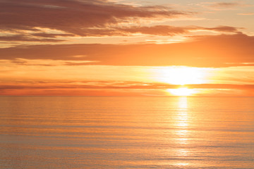 Fototapeta na wymiar Bright golden dramatic sunset sun reflecting orange, gold, off calm ocean
