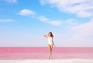 Fototapeta na wymiar Beautiful woman in swimsuit posing near pink lake on sunny day