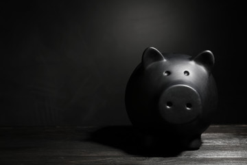 Black piggy bank on table against dark background with space for text. Poverty concept