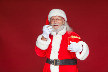 Christmas. Smiling, kind Santa Claus in white gloves with his mouth open holds a red bucket with popcorn with one hand, takes some popcorn and prepares to eat it with the second hand. The concept of