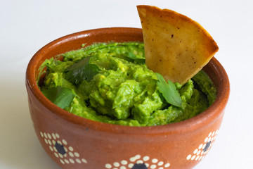 Guacamole mexicano tradicional de la salsa en el cuenco de arcilla y nachos en el fondo blanco