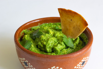 Guacamole mexicano tradicional de la salsa en el cuenco de arcilla y nachos en el fondo blanco