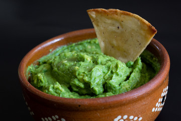 Guacamole mexicano tradicional de la salsa en el cuenco de arcilla y nachos en el fondo de un tablero de pizarra