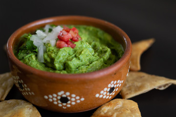 Guacamole mexicano tradicional de la salsa en el cuenco de arcilla y nachos en el fondo de un tablero de pizarra
