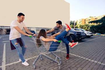 YOUNG FRIENDS HAVING FUN ON A SHOPPING TROLLEY. Young and careless friends concept.