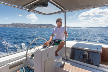 Attractive male skipper navigating the fancy catamaran sailboat on sunny summer day on calm blue...