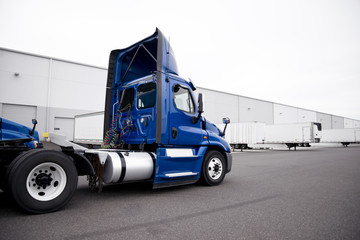 Big rig day cab blue semi truck driving to warehouse dock for pick up the semi trailer