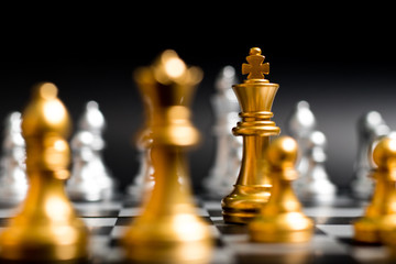 Gold king and team in chess game face with the another silver team on black background (Concept for company strategy, business victory or decision)