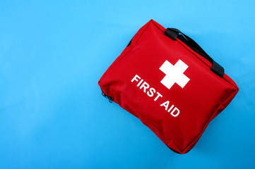 First aid treatment and medical emergency response concept with flat lay view of a red with a white cross first aid kit isolated on blue background with copy space for text