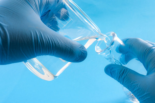Scientific experiment, chemical reaction and experimental chemistry concept with close up on the hands of a scientist wearing blue rubber gloves and pouring liquid chemicals from a flask in test tube