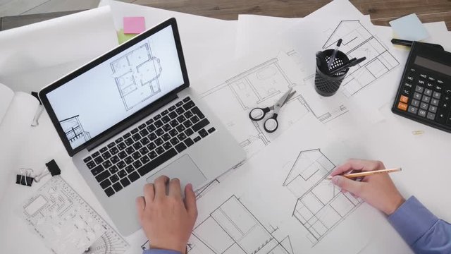 Top view of a male architect working on laptop computer with blueprints on screen