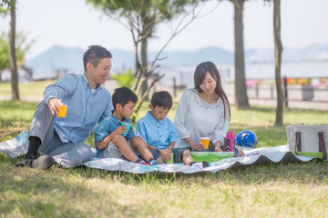 公園でレジャーシートに座りピクニックをする家族