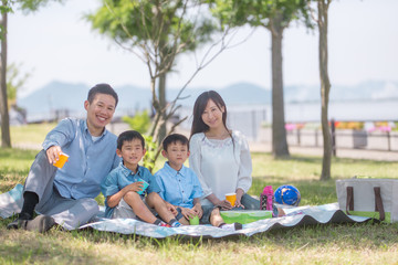 公園でレジャーシートに座りピクニックをする家族