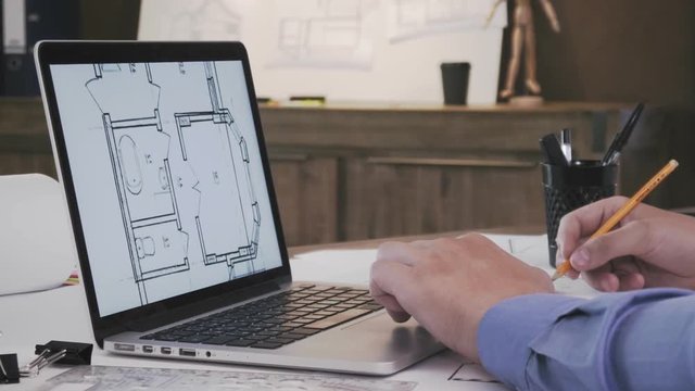 Architect working with blueprints on laptop computer