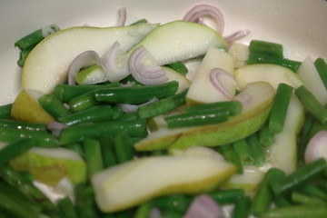 Sliced pear, chopped broccoli, and sliced red onion in a pan.  Searing ingredients on a flat top oven.