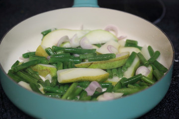 Sliced pear, chopped broccoli, and sliced red onion in a pan.  Searing ingredients on a flat top oven.