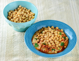 Close up dish fresh hummus and tahini topped with olive oil, pepper,lemon, chickpea seed on white tablecloth background. Hummus Traditional Middle Eastern food commonly served in a pita. Copy space.