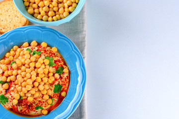 Overhead image dish Chickpea hummus and tahini dipped with olive oil, pepper, parsley, spices on a white table background. Hummus Traditional Middle Eastern food commonly served in a pita. Copy space.