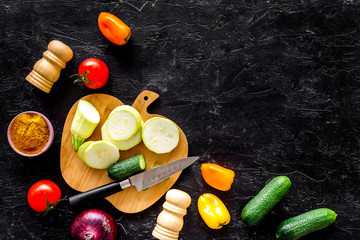 Cooking vegetable stew concept. Fresh vegetables squash, bell pepper, tomato, spices and cutting doard on black background top view space for text