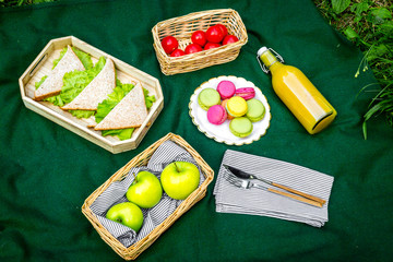 Food for picnic on tablecloth on green grass. Meal outdoor concept. Sandwiches, vegetables, sweets, drinks top view
