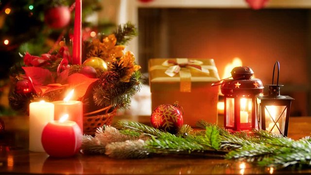 Closeup video of beautiful decorated christmas table with candles and gifts against glowing Christmas tree and burning fireplace