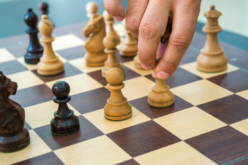 Hand moving a wooden chess figure on a chess board