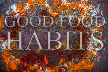Spices powder on brown colored wooden surface including salt and pepper with written Good Food Habits on it.