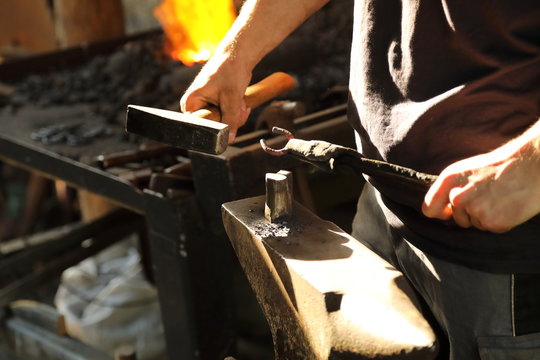 The blacksmith works with anchor metal on an anvil with a hammer and ticks - Powered by Adobe
