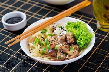 Vegan noodle soup with tofu cheese, shiitake mushrooms and lettuce in white bowl. Asian food.