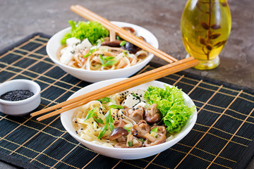 Vegan noodle soup with tofu cheese, shiitake mushrooms and lettuce in white bowl. Asian food.