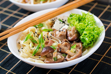 Vegan noodle soup with tofu cheese, shiitake mushrooms and lettuce in white bowl. Asian food.