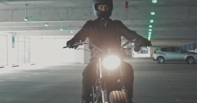 Motorbiker riding on a motorcycle in the parking lot in the city. Biker rides a vintage custom motorbike from 1970s in the garage. 4K video shooting by handheld gimbal