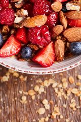 Close up of natural fresh ingredients for healthy breakfast strawberry, blueberry, almonds, granola in a white bowl on a wooden background.