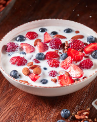 Dietary homemade natural breakfast with fresh organic ingredients - berries, granola, nuts and milk in a white bowl on a wooden table.