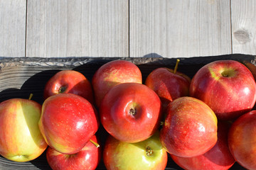 Red shiny apples in pottery dish on grey natural wooden background with copy space for text outdoors in sunlight.  Freshly harvested sweet tasty fruit as healthy snack or for preparing salad cooking o