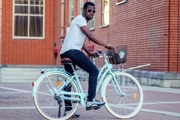 Obraz premium handsome African American man stylish well-dressed standing with a blue bicycle red brick building background . sports ecological transport concept