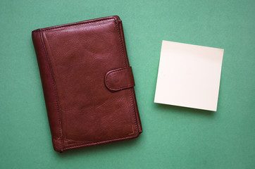 Brown wallet and blank paper sheet isolated on green background.