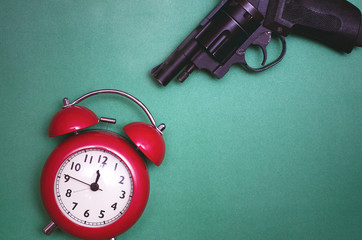 Red alarm clock and handgun isolated on green background. The waste of time concept. Kill the time.