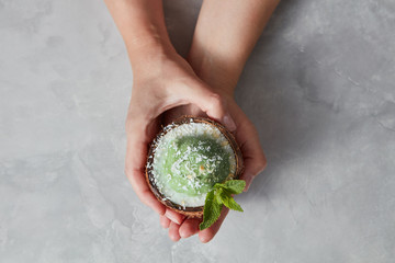 Womans hands take a halh of coconur with tasty homemade green ice cream with mint leaf on a gray...