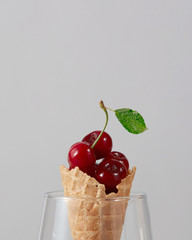 Sweet wafer cone with freshly picked red cherries in a glass on a gray background.