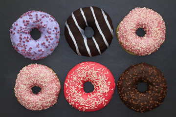 Donuts of different colors on dark background, view from above 