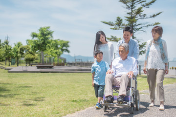公園で微笑む車椅子のシニア男性と三世代家族