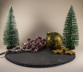 Weihnachtliche Deko-Elemente auf einer runden schwarzen Platte. Zwei Tannen, eine Christbaumkugel,...