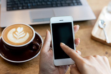 hand woman using a telephone, empty screen smart phone and computer on wooden table In the coffee shop.