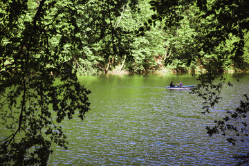 The Green Lake of Hamori in Lillafure near Miskolc, Hungary. Spring landscape with sunrays covering the mountains. The solar path on the water. Unrecognizable people on boat