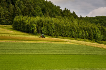 Obraz premium Field work, the tractor overturns the drying hay