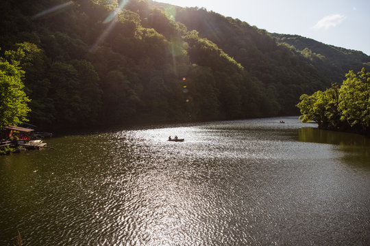 The Green Lake of Hamori in Lillafure near Miskolc, Hungary. Spring landscape with sunrays covering the mountains. The solar path on the water. Unrecognizable people on boat