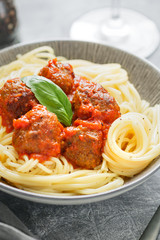 Beef meatballs in tomato sauce with Italian spaghetti and fresh basil leaf on a dinner table. Simply homemade recipe.